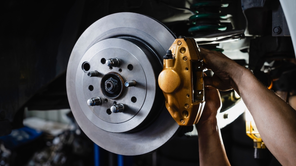 The hands of a white man working on the brake rotors of a vehicle