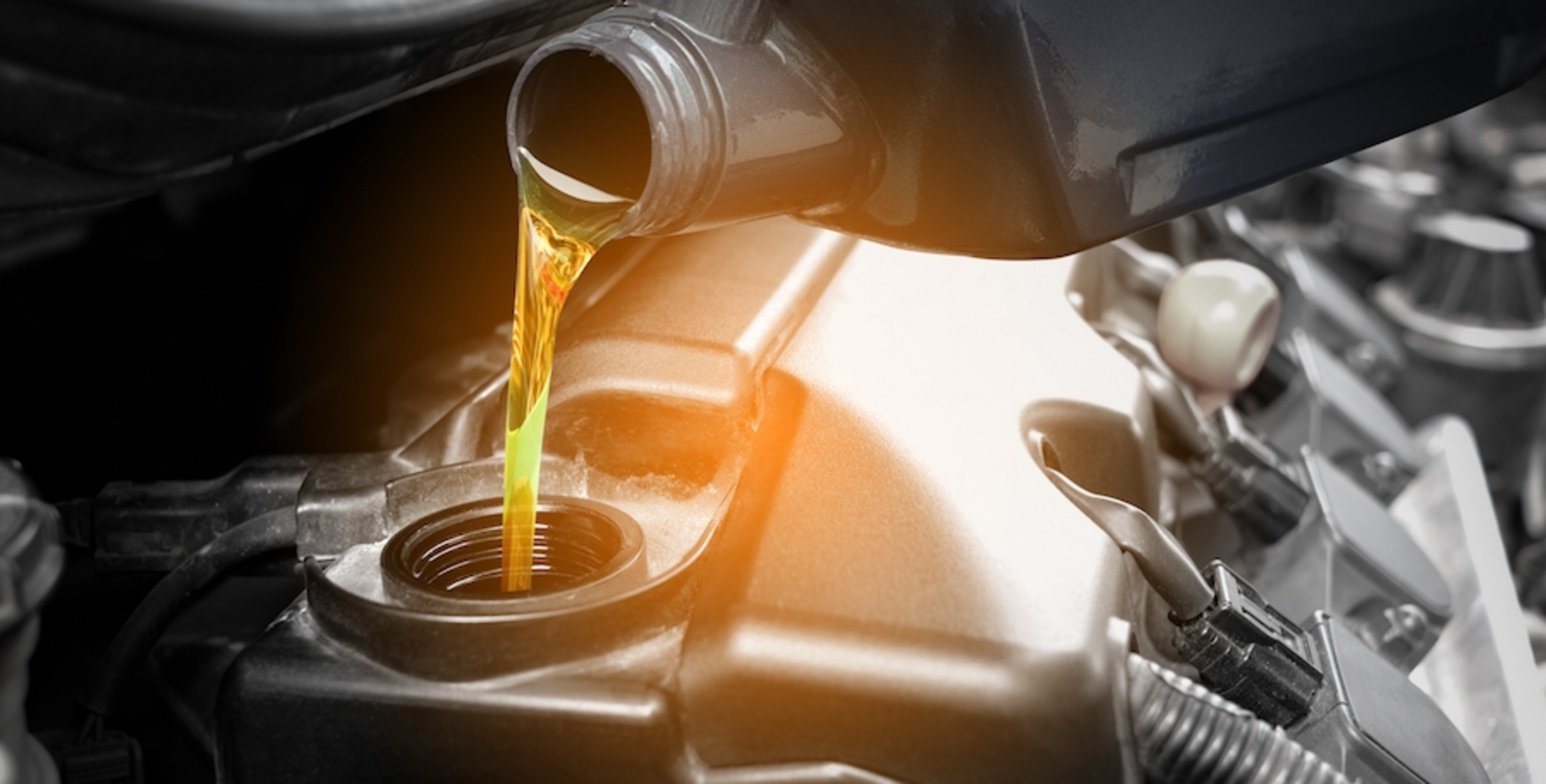 Yellow oil being poured from a gray bottle into a vehicle’s engine