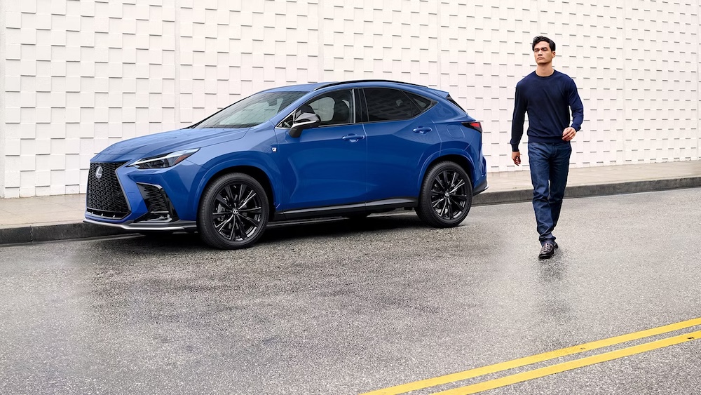 A man walking away from a blue 2026 Lexus NX SUV parked beside a gray wall
