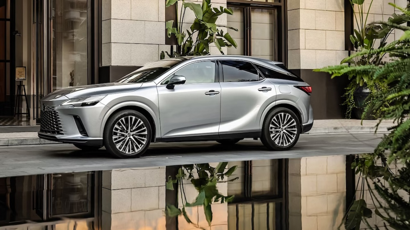 A side view of a silver 2026 Lexus RX hybrid SUV parked beside a reflecting pool