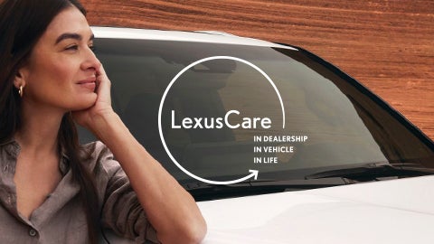 Woman looking into the distance beside a parked Lexus vehicle.
