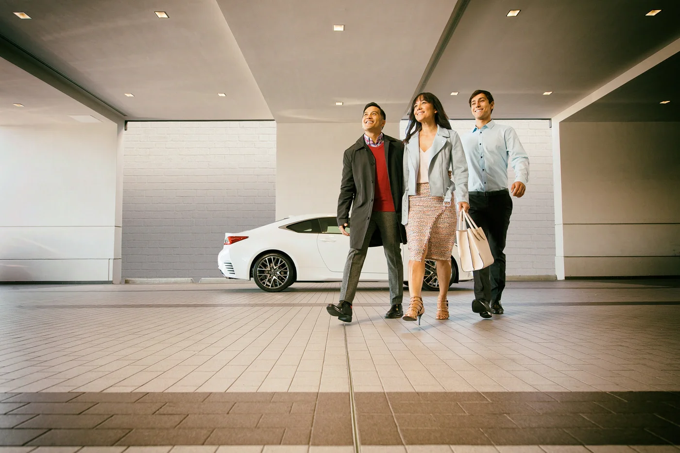 Three people, two men and a woman, walk away from a white Lexus