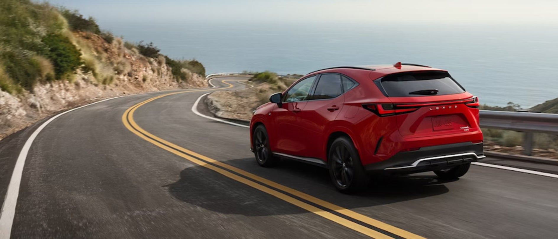 A red Lexus NX PHEV driving down a winding road towards the water
